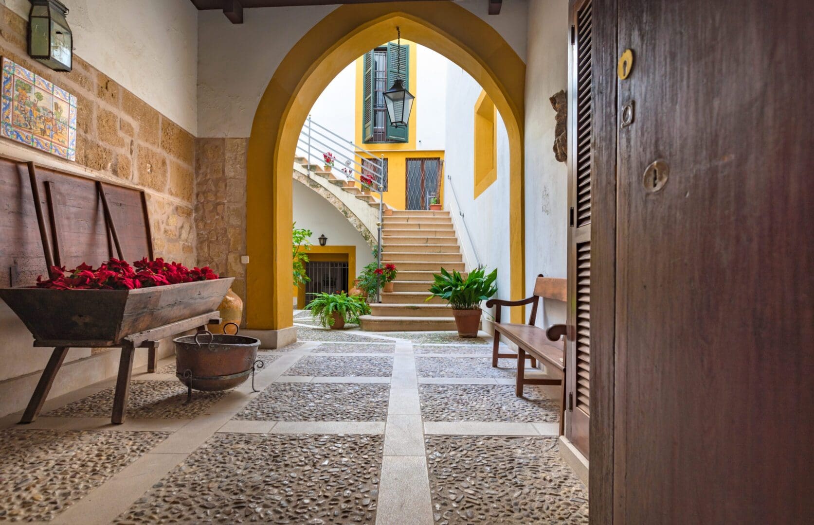Sunlit arched courtyard with stairs and potted plants
