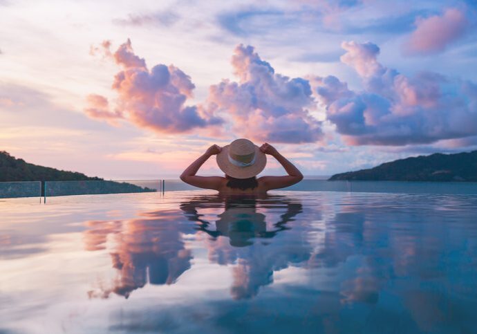Person in infinity pool wearing hat at sunset